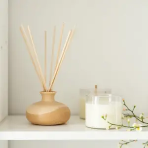 A wooden diffuser next to two candles on a white shelf.