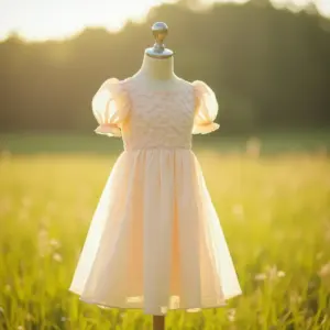 A pastel pink dress displayed on a mannequin in a sunlit field.