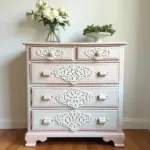 Vintage dresser with floral decor and intricate carvings. Fresh flowers in a vase on top.